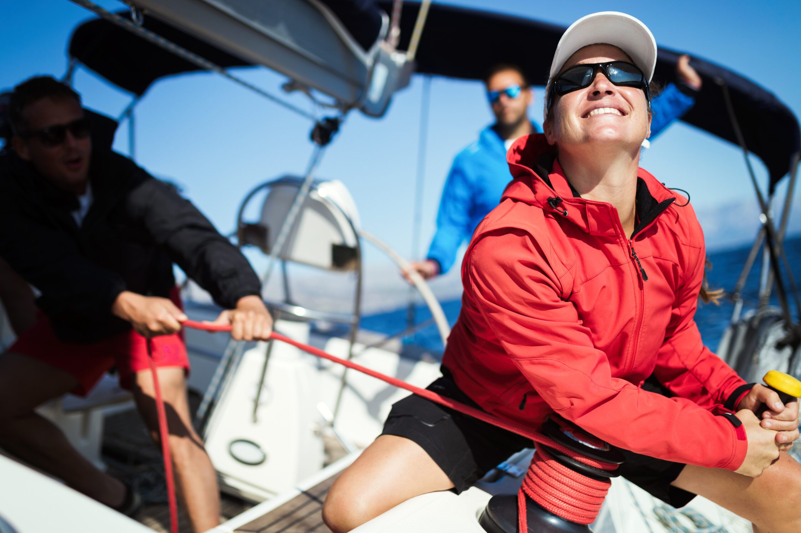 woman in a red jacket, smiling, and sailing a boat